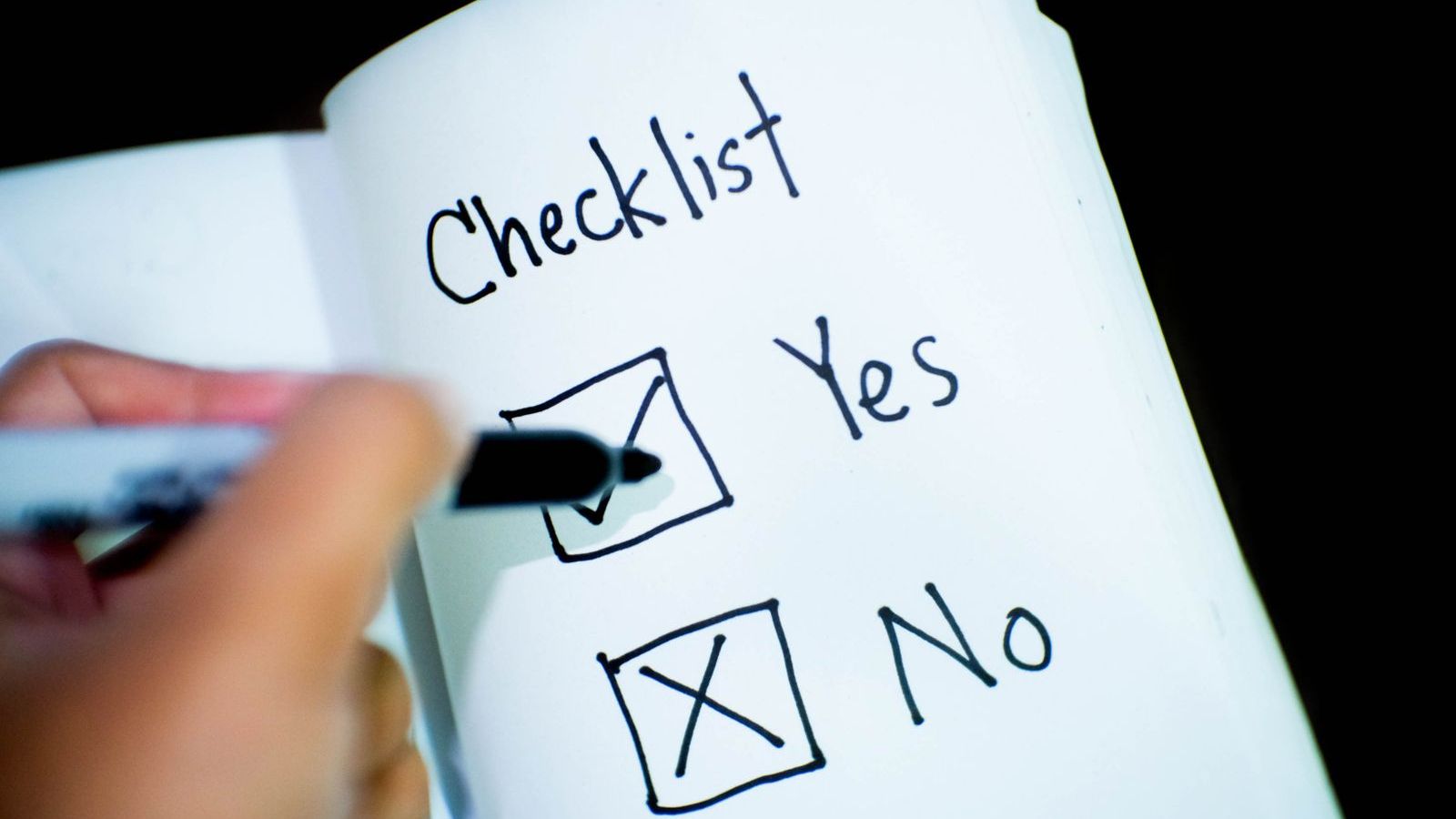 Person ticking items on a checklist in a book, representing a buyer checklist for choosing field force software