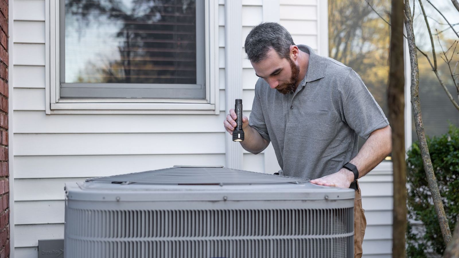 Technician inspecting an outdoor air conditioning unit, representing maintenance rounds in facility management