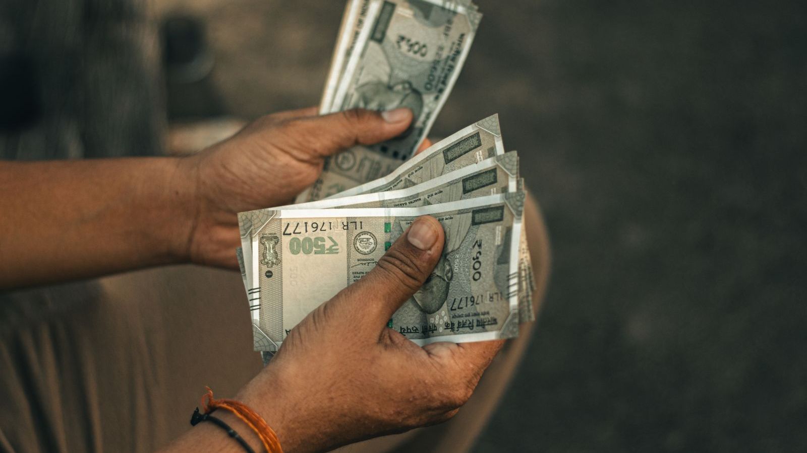 Hands counting Indian rupee notes, representing cash collections by field teams