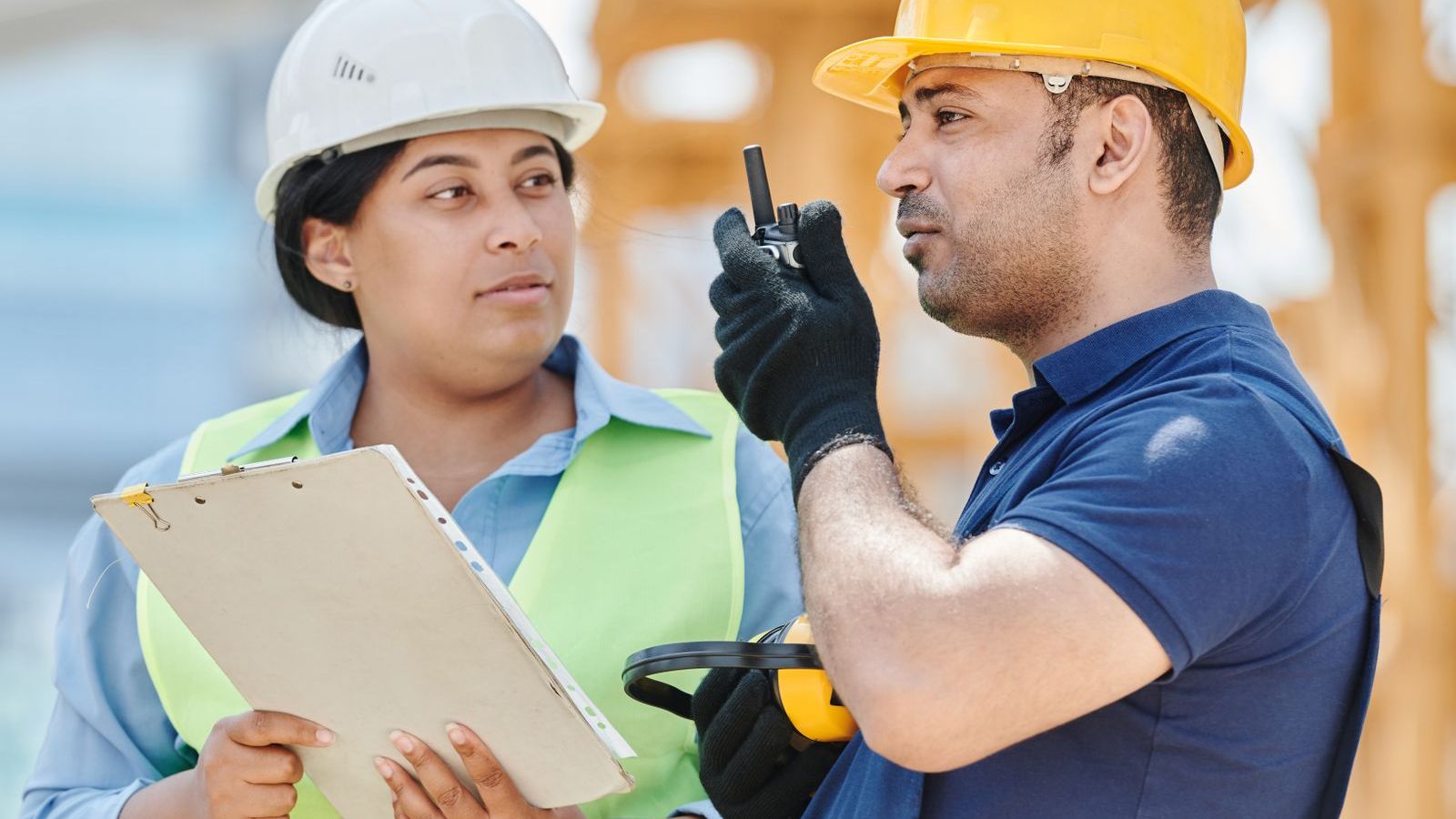 Two construction workers in hard hats with a clipboard and radio on a building site