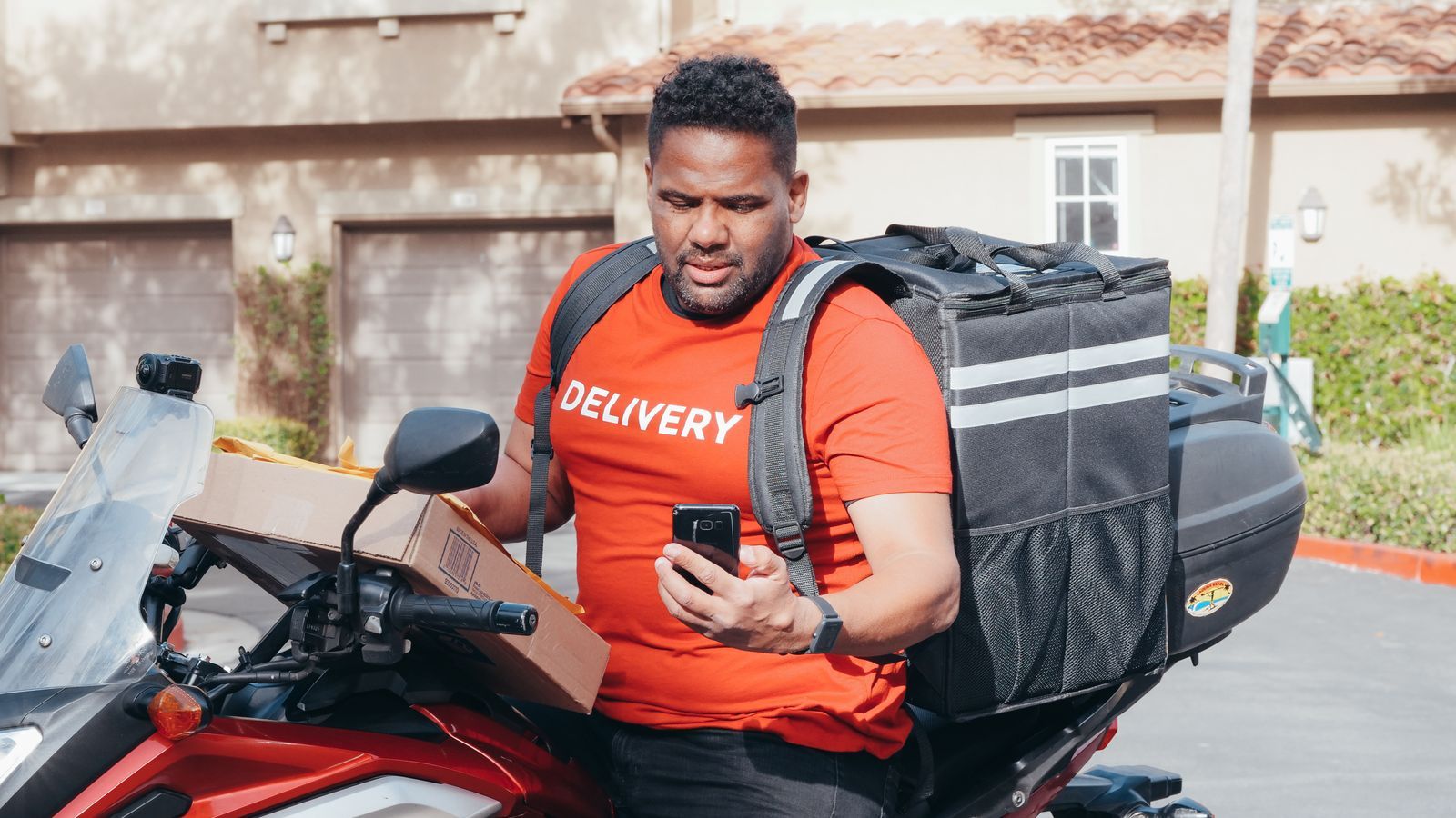 Delivery rider on a motorcycle checking a smartphone, representing live GPS tracking of field employees