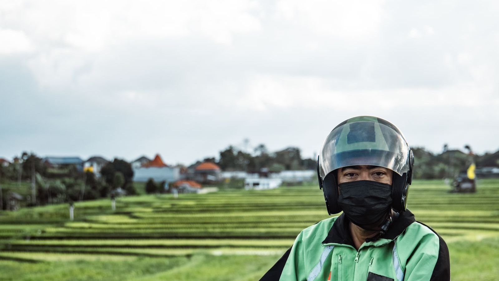 Delivery rider on a motorbike on a rural road with green fields, representing field work in low-connectivity areas