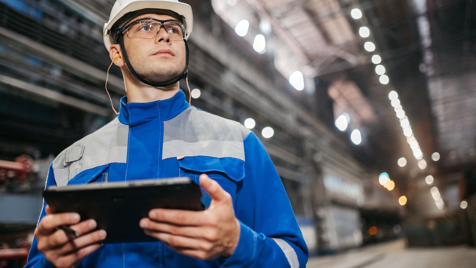 Engineer in safety gear holding a tablet in a factory, representing SLA tracking for field service teams